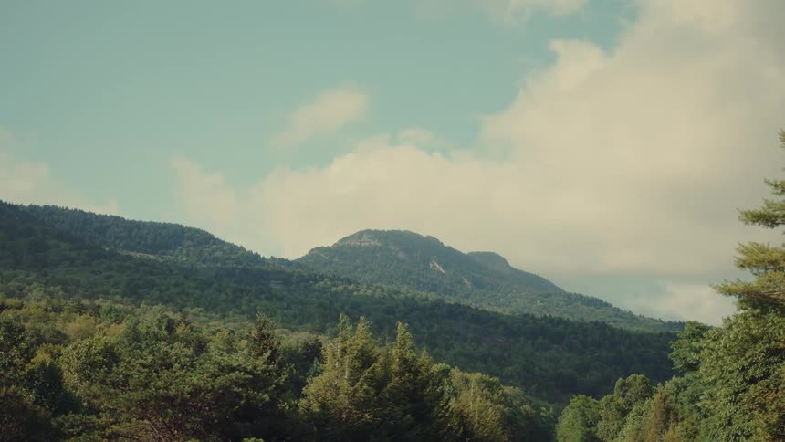 A scenic landscape shot captures a lush forested mountain under a partly cloudy sky