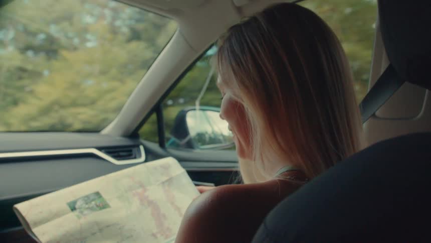 A woman navigates with a paper map in the passenger seat of a moving car