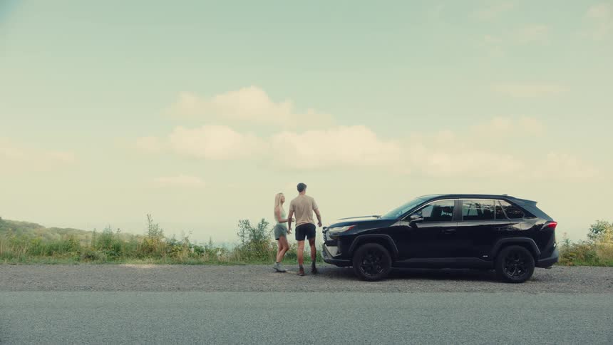 Man and a woman getting out of a black car and hugging in front of a landscape