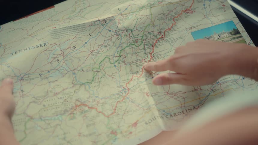A woman holding a map while sitting in a car looking at it and pointing to a road on the map