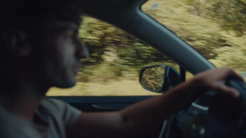 Man drives a car on a road with trees passing by