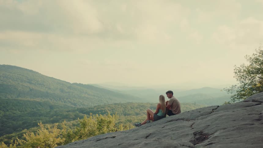 Woman and a man sitting on a rock with mountainous landscape