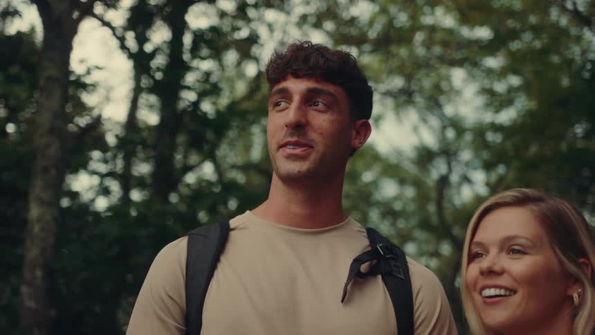 A man and a woman together in an area with many trees talking and pointing at something