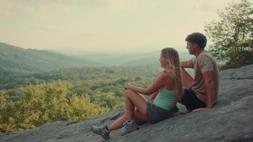 A man and woman sit on the mountain looking over the landscape