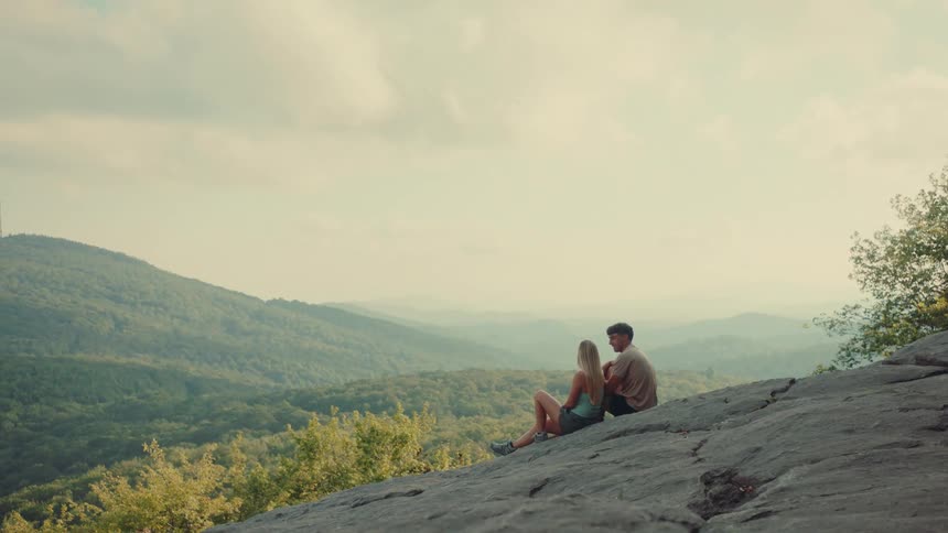 Couple sitting on a rock with a view of mountains during the day
