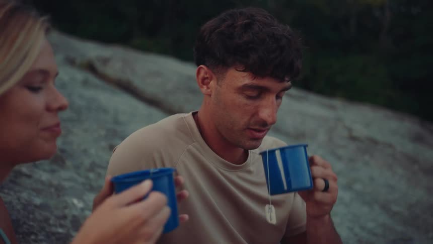 Man and a woman having a drink from blue cups while standing outdoors