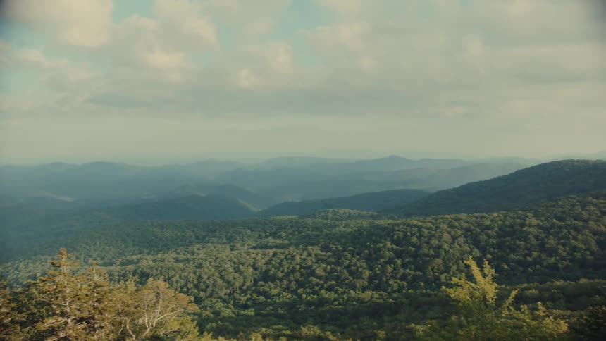 Panoramic view of a mountain range covered with forests under a partly cloudy sky