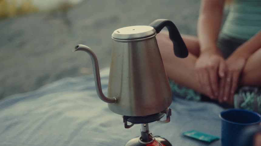 Teapot on a portable outdoor stove with a woman sitting next to it