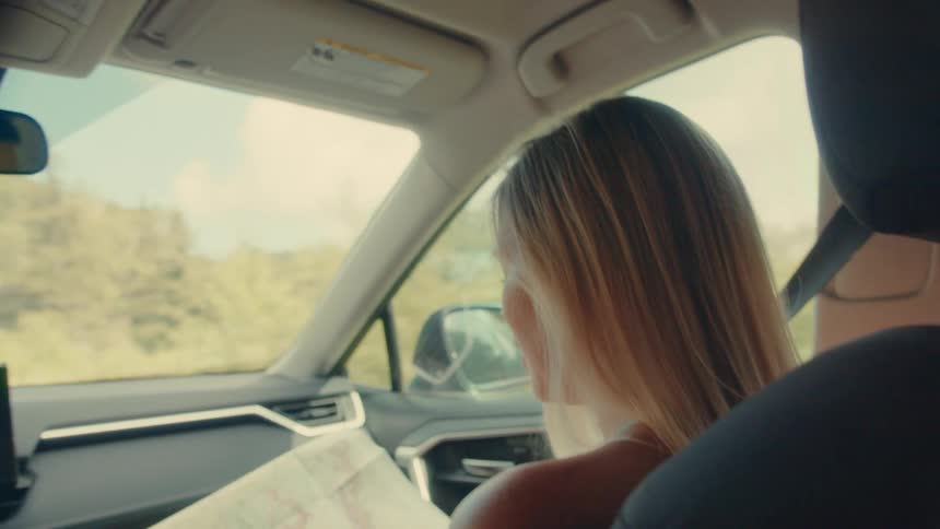 Blonde woman in the passenger seat of a moving car holding a map