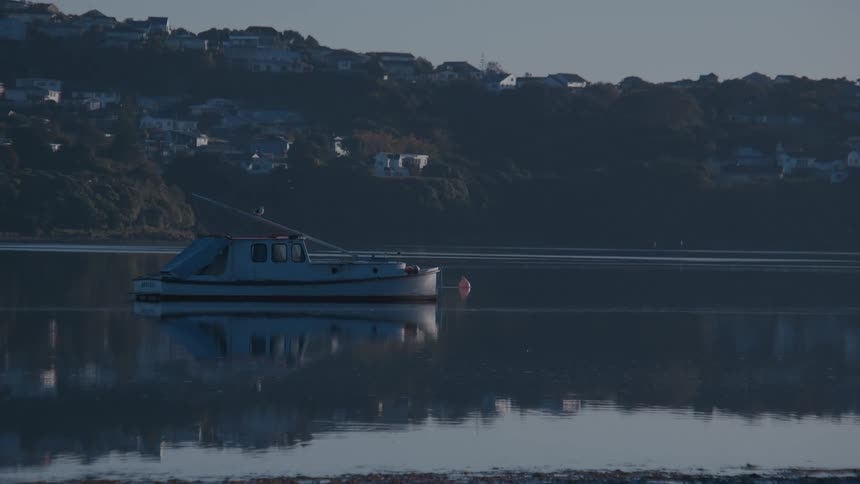 Weathered boat sits on reflective water while haze covers the houses on the coast in the background