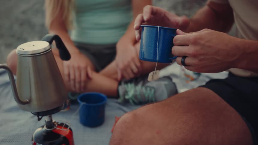 Pair of hands of a man accompanied by a woman preparing tea in an outdoor setting