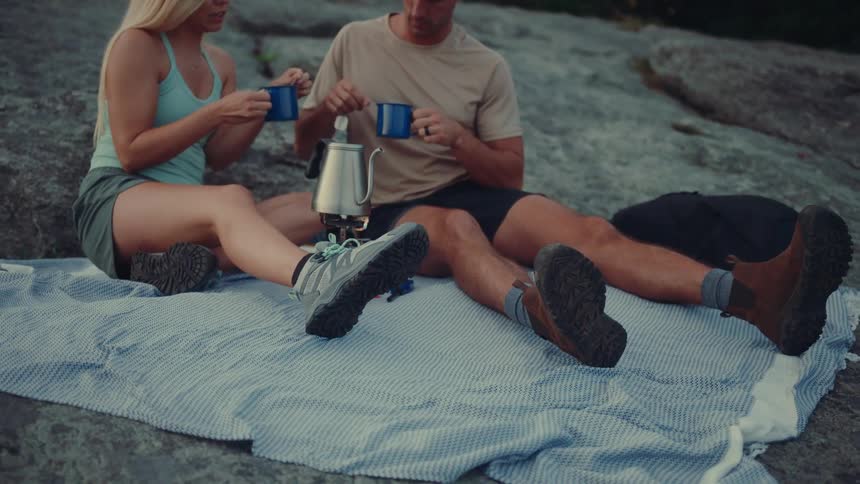 Man and a woman sitting on a scarf on a rock drinking a cup of tea