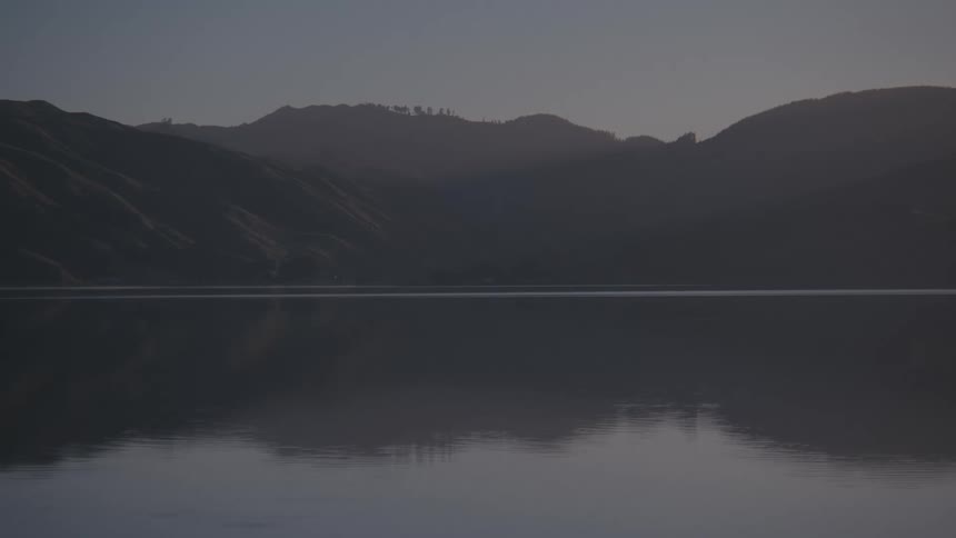 Calm lake surrounded by mountains at sunrise