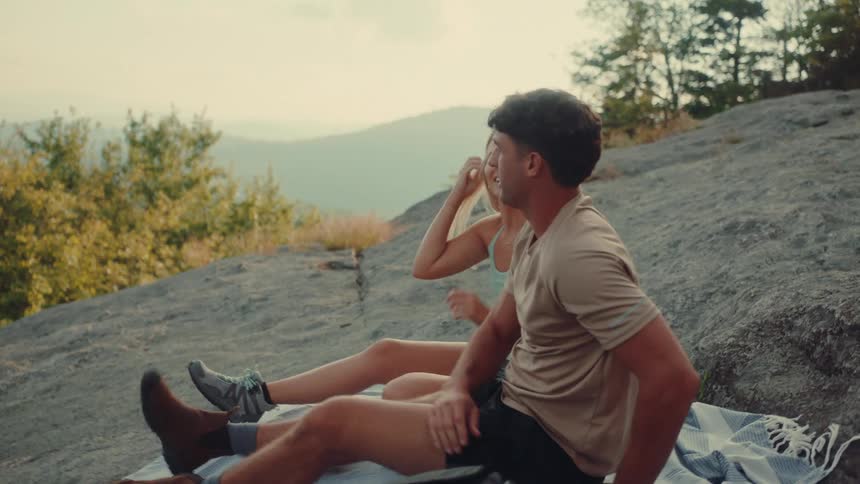 Couple hiking on a mountain placing a scarf on a rock and sitting down