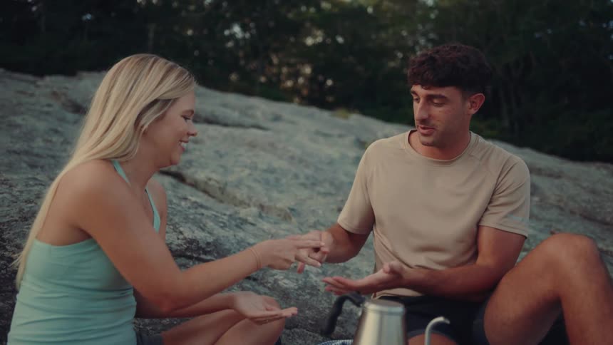 Couple sitting outdoors playing rock paper scissors on a picnic blanket