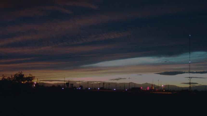 City lights glow faintly beneath layered twilight clouds and distant mountains