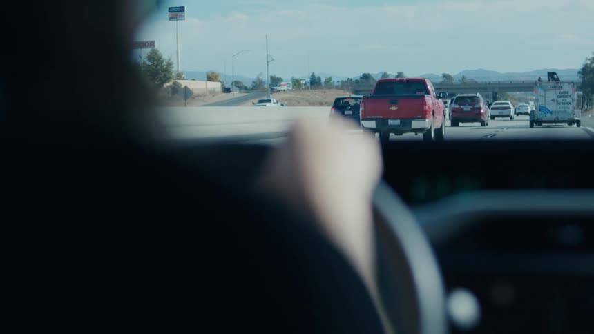 Person with hands on steering wheel driving a car on a highway during the day