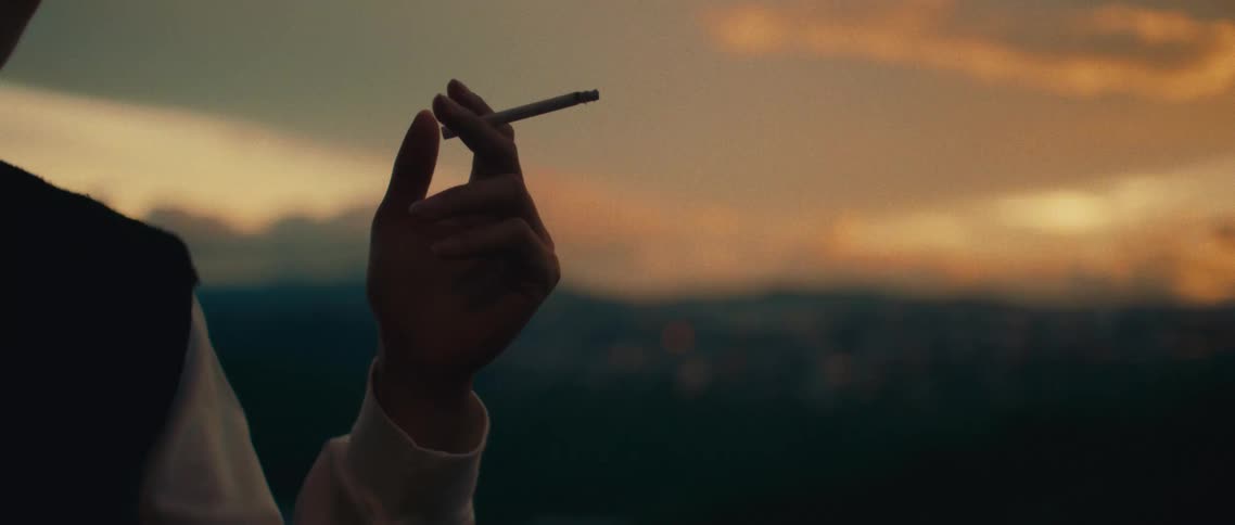 A hand holds a cigarette in the fading light of sunset casting a contemplative mood