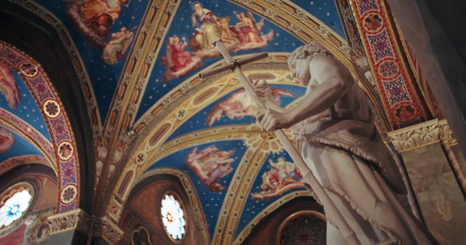 A detailed shot inside a church featuring a prominent stone statue of a saint in the foreground and a magnificent intricately painted vaulted ceiling with frescoes of angels and celestial scenes in the background