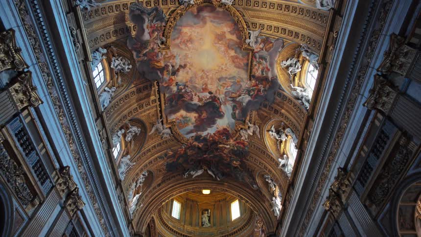 An upward view captures the lavish frescocovered ceiling of a grand baroque church bathed in soft natural light