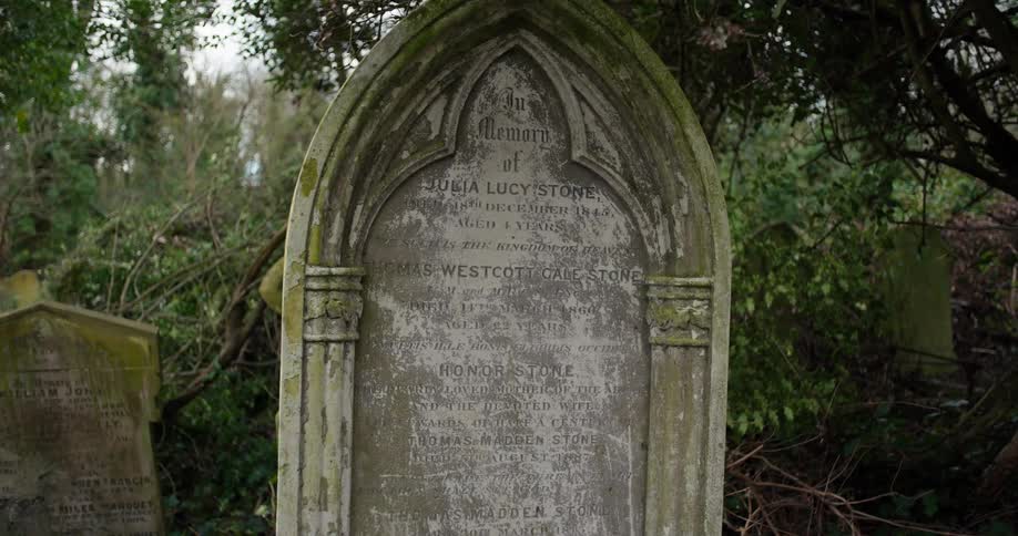 Old stone gravestone with english inscriptions surrounded by vegetation in a cemetery