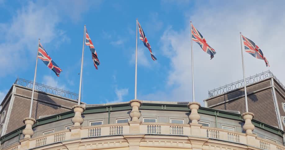 A series of england flags flying on top of a curved building roof at midday