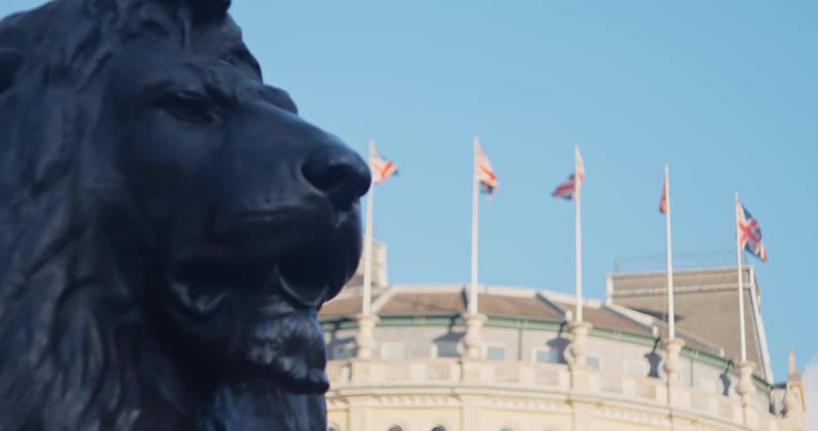Bronze statue of a lion in the foreground and a building with uk flags in the background