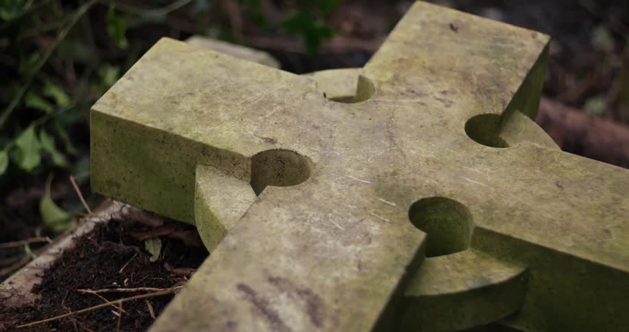 Fallen stone cross on the ground covered with moss among vegetation