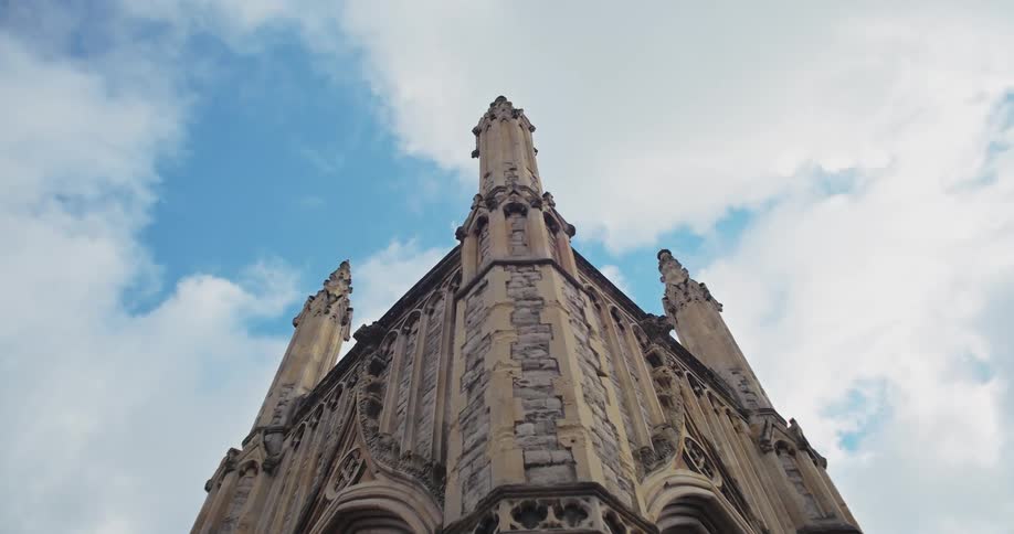 The video shows a lowangle shot of a gothicstyle building which appears to be a church or a similar historic structure the facade is highly detailed with intricate carvings spires and pointed arches made of stone the sky is a mixture of blue and wh