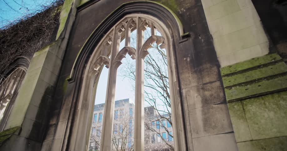 Gothic window ruins with a view of trees and a modern building in the background