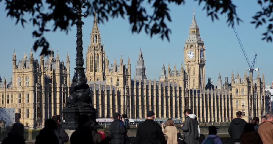 People walking along the riverside with a view of the palace of westminster and big ben in the background