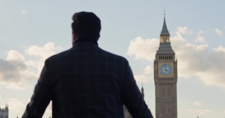 Man seen from behind looking at big ben in london under a partly cloudy sky