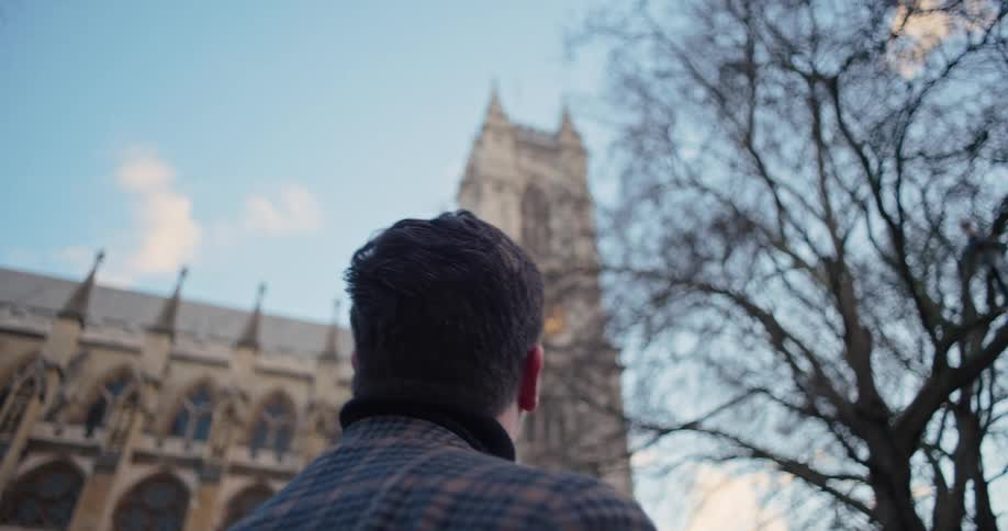 The man is walking and looking up at the large stone church