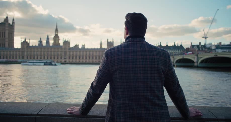 Man seen from behind leaning on the railing overlooking big ben and the houses of parliament in london