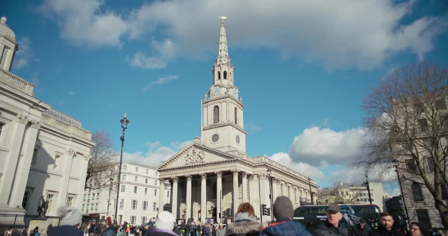 A busy street with people walking by and st martininthefields church visible in the distance at midday