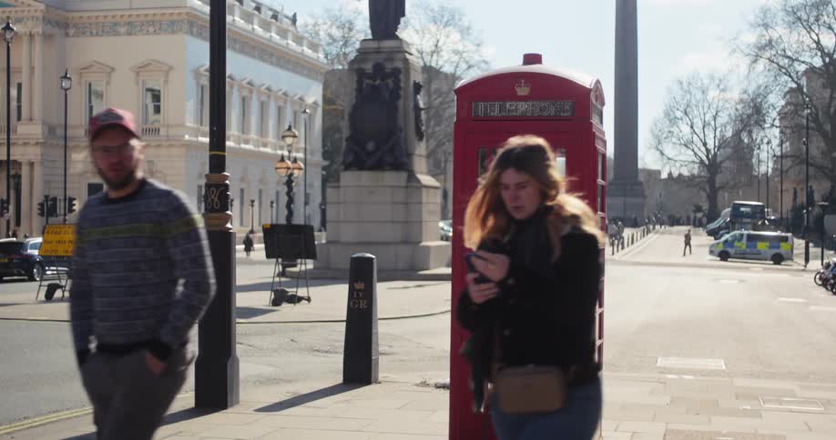 Two people walk past a phone booth on the sidewalk in the city at midday