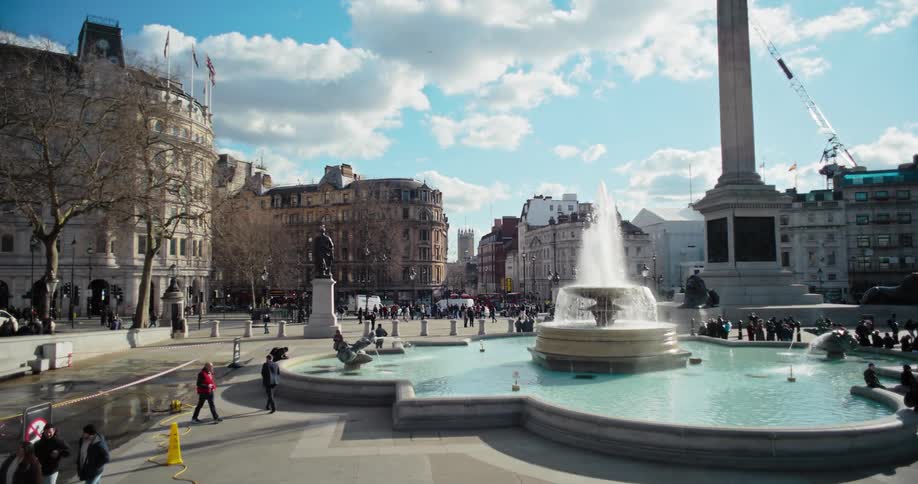 A fountain in a public park in the city as a series of people walk by it at midday