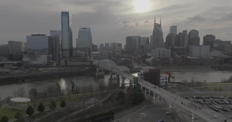 Aerial view of a city with skyscrapers a bridge over the river and the sun partially covered by clouds in the background