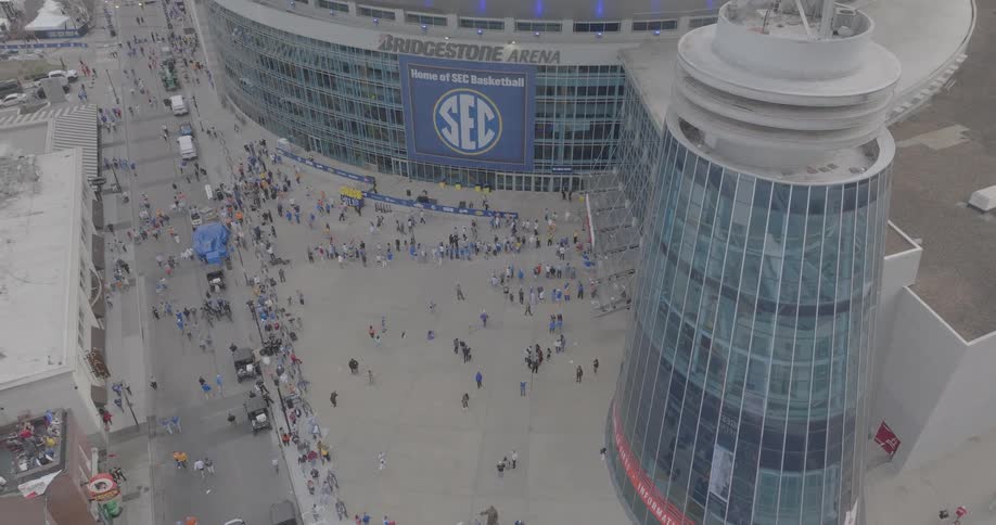 A daytime aerial view shows crowds gathering outside bridgestone arena in nashville with sec basketball signage prominently displayed
