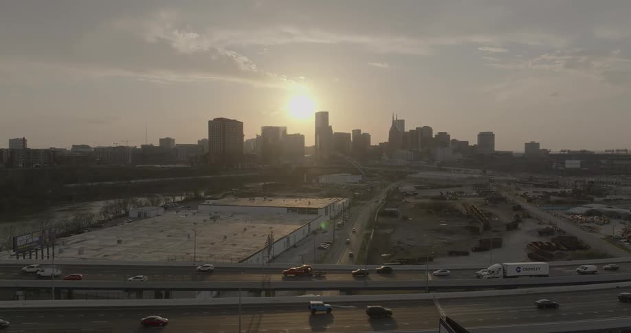 A long bridge linking two cities as cars go by with the orange sunset behind the citys skyscrapers and highrise buildings