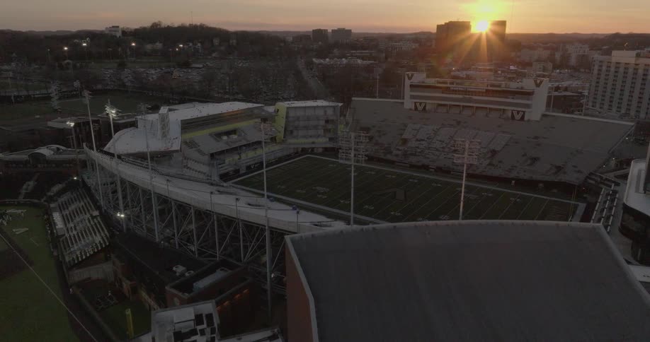 An aerial view of vanderbilt stadium at sunset shows the empty stands and quiet field silhouetted against the glowing skyline of nashville
