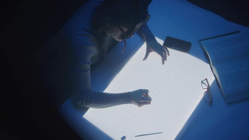 Woman draws on a grid on a lightbox in a dim room