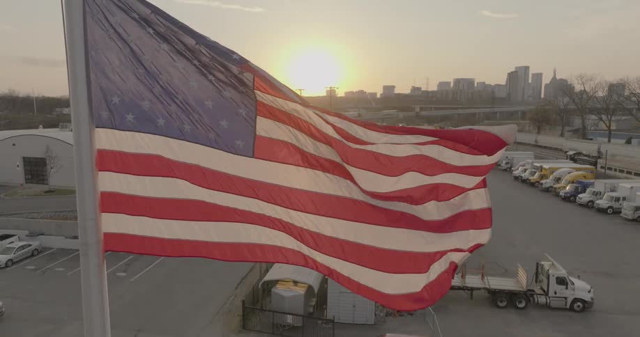 A flag flaps in the wind over a parking lot full of trucks in front of a city