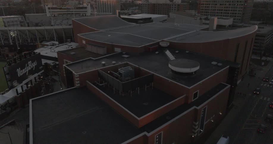 The camera slowly zooms out from a large brown brick building with a curved roof revealing a stadium and other city buildings under a dim hazy sky