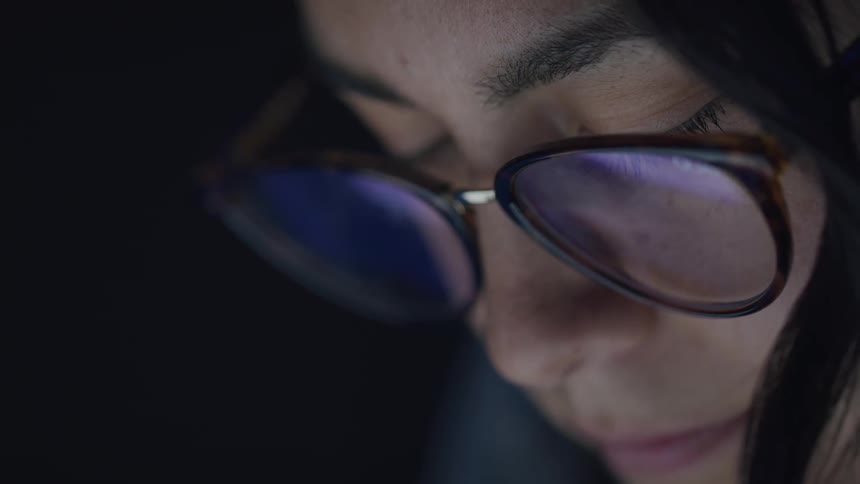Focused woman blinks while her eyeglasses reflect a device