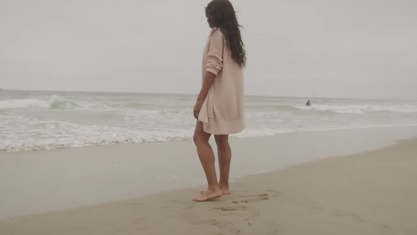 A barefoot woman standing on the beach sand contemplating the sea