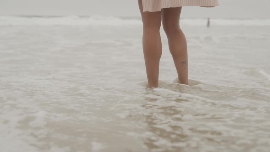 A woman at the edge of the beach with her bare feet in the seawater