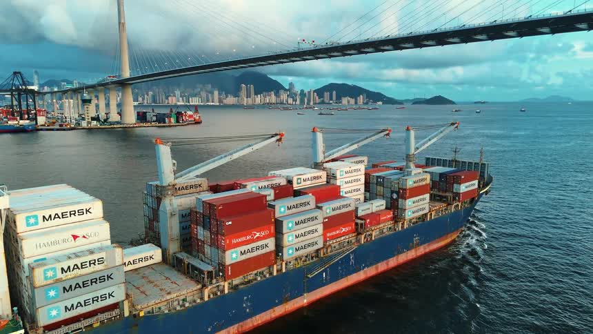 Maersk container ship sailing under a large bridge loaded with multiple colorful containers