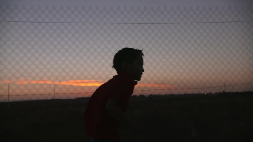 A silhouetted boy runs along a fence at sunset