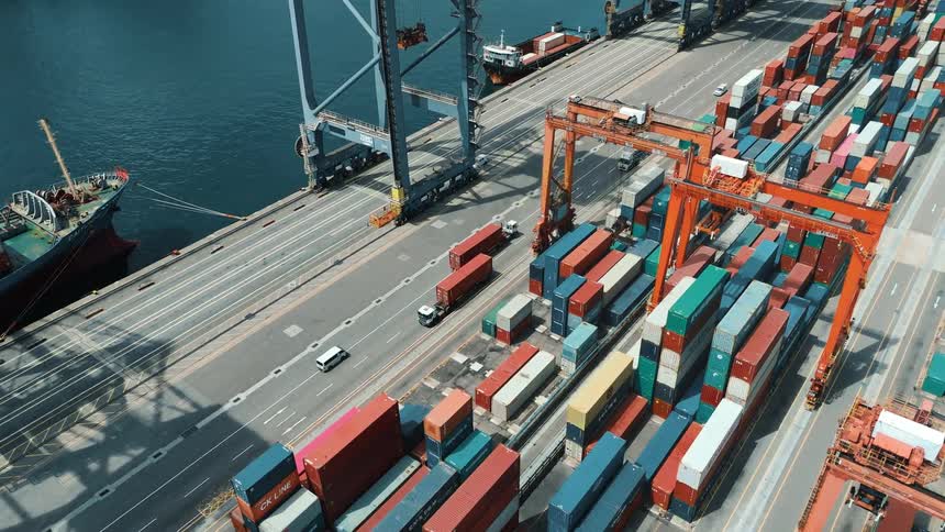 A seaport filled with containers at midday with cars and shipping trucks driving by